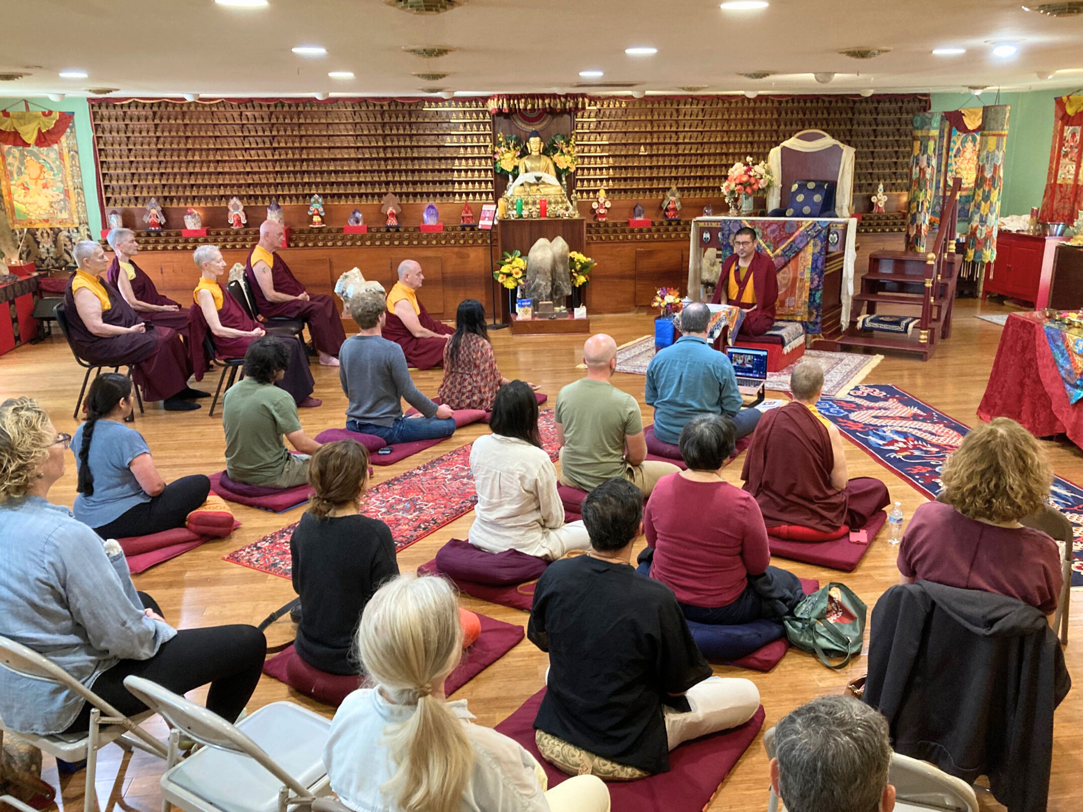 Khenpo Karze teaching a full meditation class in KPC's Prayer Room, with an audience of lay students, monks and nuns, some seated in chairs and some on cushions on the floor.