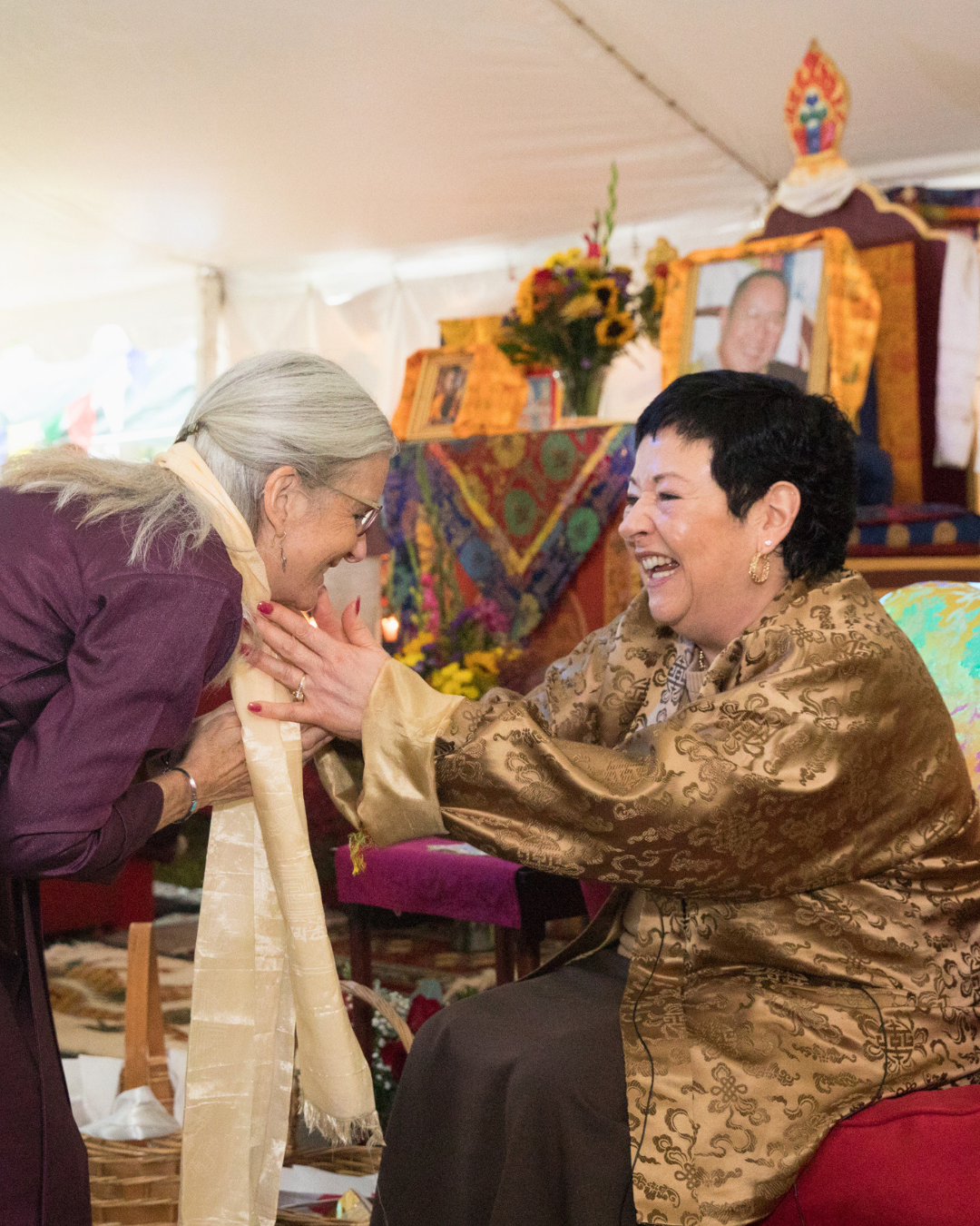 Jetsunma Ahkön Lhamo, smiling warmly, places a white silk blessing scarf (khatag) around the neck of a student during her 30th Enthronement Anniversary celebration in 2018.